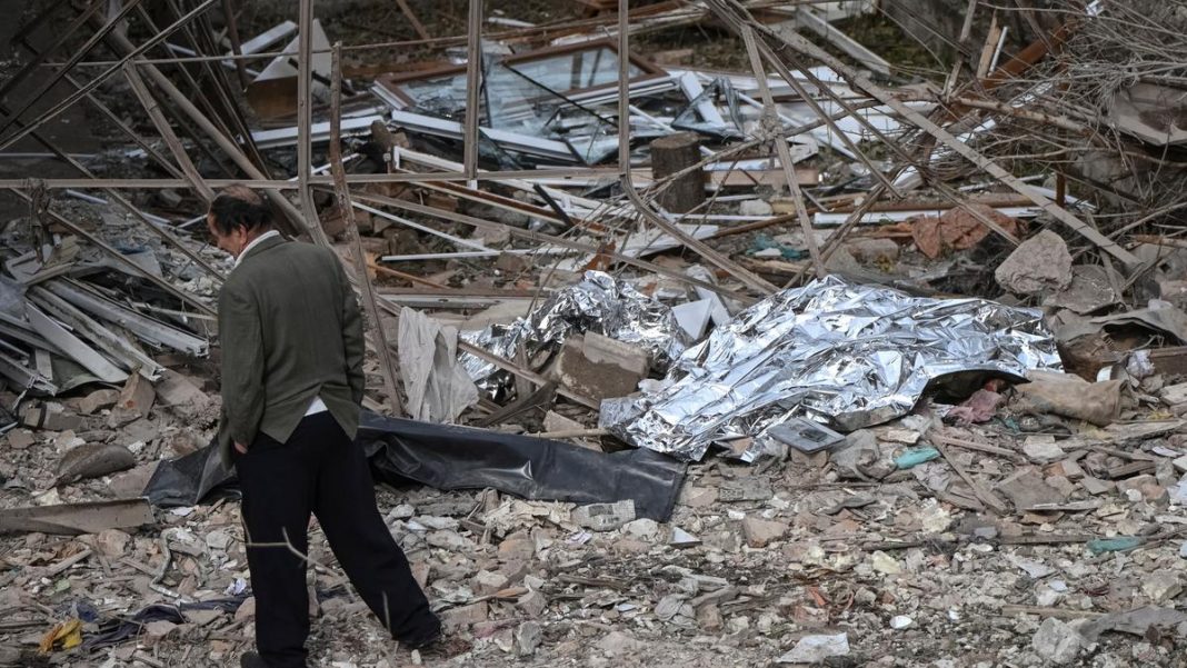 A man walks near the covered bodies of the victims of a Russian drone and missile strike, lying near their destroyed house, amid Russia’s attack on Ukraine, in the village of Lapaivka on the outskirts of Lviv. | Photo Credit: Reuters