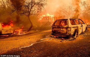 Global temperature increases boost the risk of catastrophic events such as droughts and intense wildfires. Pictured, Molten metal from a burned car meanders on the road as flames engulf a home during the Thompson fire in Oroville, California on July 2, 2024
