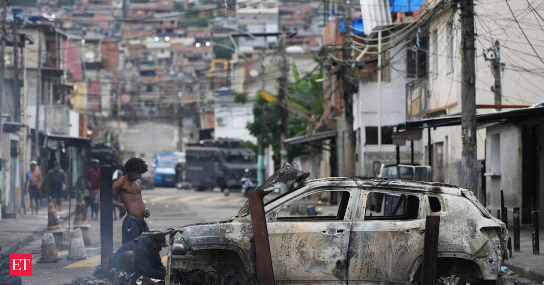 People remove useful parts from a burned car used as a barricade by alleged drug traffickers during a police operation in the Complexo do Alemao favela where the criminal organization 