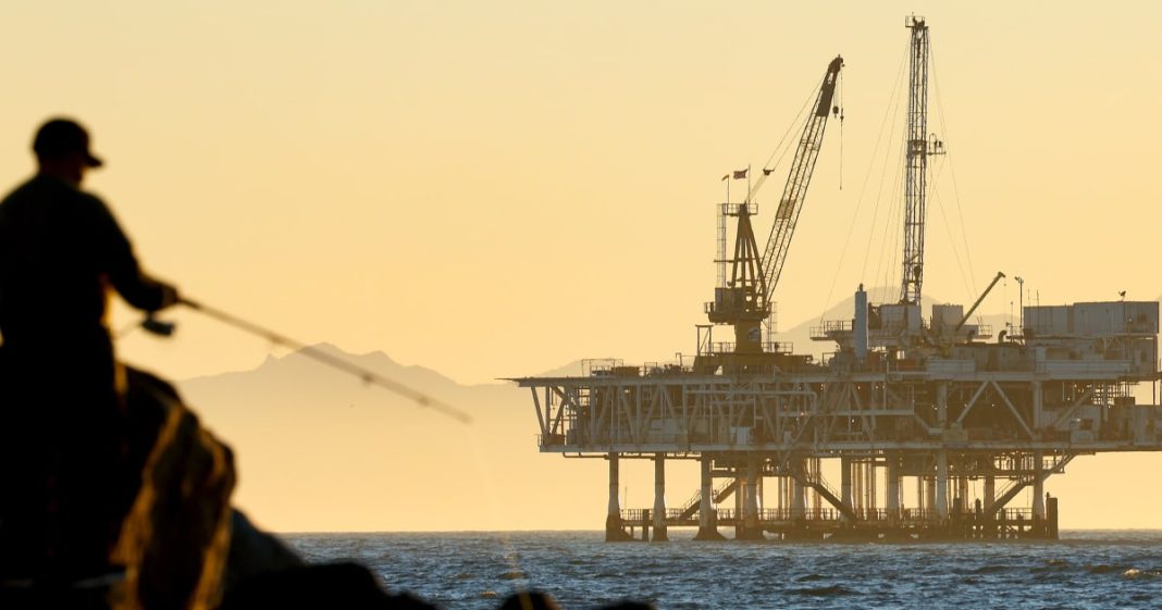 A person fishes in Seal Beach, Calif., with the offshore oil and gas platform Esther in the distance,