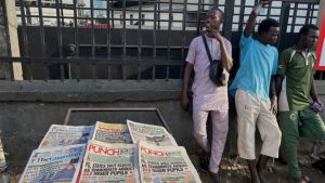 People stand near a display local newspapers on the street of Lagos with headlines on gunmen abducting schoolchildren and staff of the St. Mary’s Catholic Primary and Secondary School in Papiri community in Nigeria, Saturday, Nov. 22, 2025. (AP Photo/Sunday Alamba )