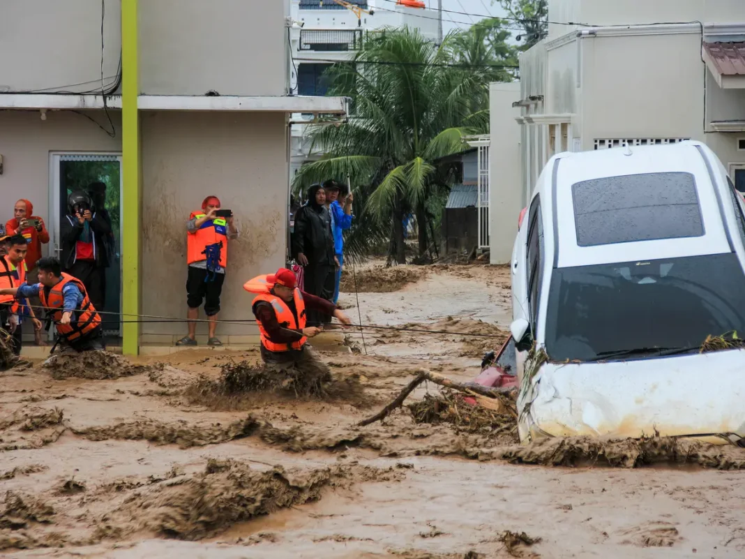 Rescuers wade through flood waters by holding a rope in their effort to evacuate residents who are trapped at their houses in Padang, West Sumatra province on November 27, 2025.