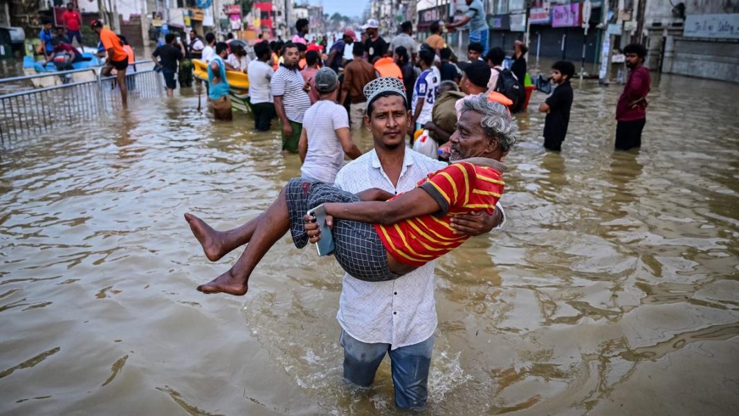 A youth carries an elderly man as they wade through a flooded street after heavy rainfall in Wellampitiya on the outskirts of Colombo on November 30, 2025. | Photo Credit: AFP
