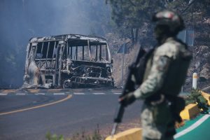 A soldier stands guard by a charred vehicle after it was set on fire following the death of El Mencho. (Photo: AP)