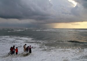 Beachgoers walk in the waters at Fort Kochi beach as clouds hover over the Arabian Sea. (Photo: Reuters)