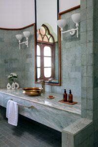 This bathroom continues the home’s Indo-Portuguese aesthetic, leaning into a more luxurious, spa-like atmosphere through stone and metal.