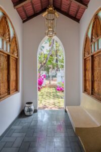 The entryway perfectly blends the home's interior elegance with its lush outdoor surroundings and continues the Goan-Portuguese architectural theme with a focus on symmetry and natural light.