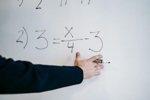 A hand writing a mathematical equation on a whiteboard with a marker. (Photo: Pexels)