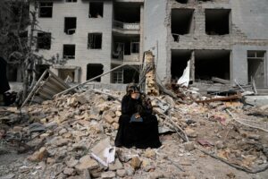 A woman sits on rubble across from a residential building damaged last Sunday during the U.S.-Israeli air campaign in Tehran, Iran, March 12, 2026.