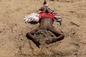 A man covers his head with sand to keep cool on a hot summer day at the Sangam. (Photo: PTI)